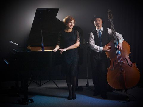 Solo pianist Yuliya Drogalova is standing in front of a black grand piano, next to her is double bassist Bartek Mlejnek